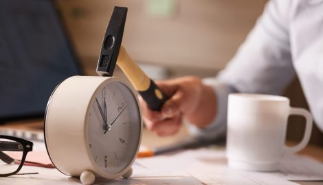 Close up of businesswoman hitting clock on her desk while working in the office.