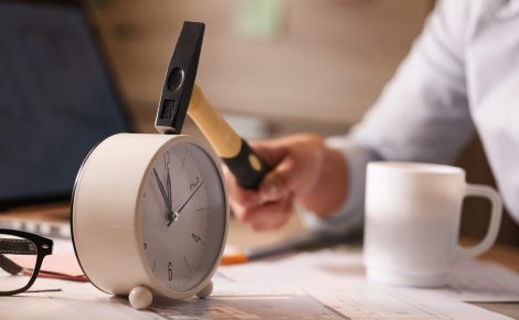 Close up of businesswoman hitting clock on her desk while working in the office.